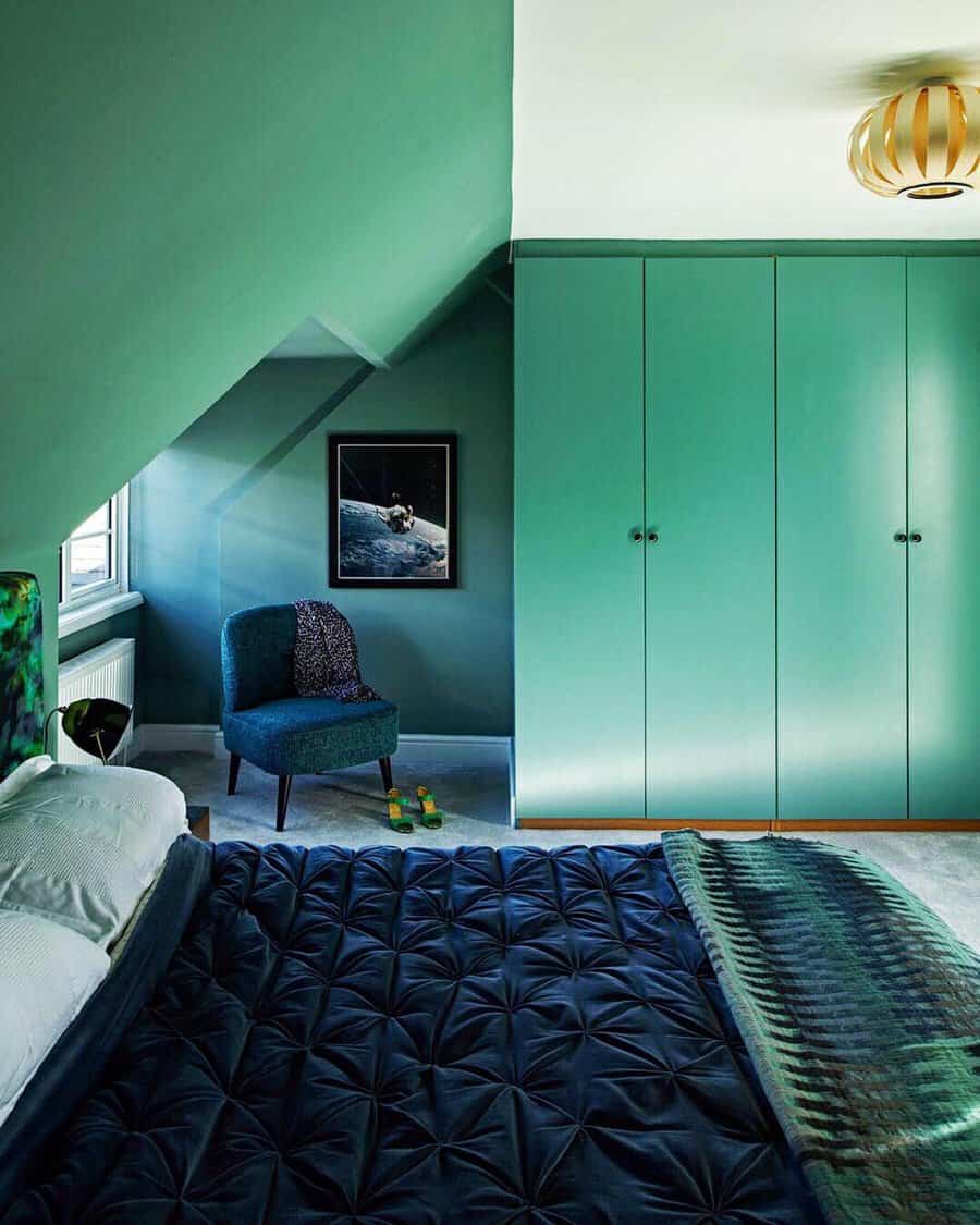 Modern bedroom with green walls and wardrobe, a navy bedspread, a blue chair, and a framed space-themed picture on the wall