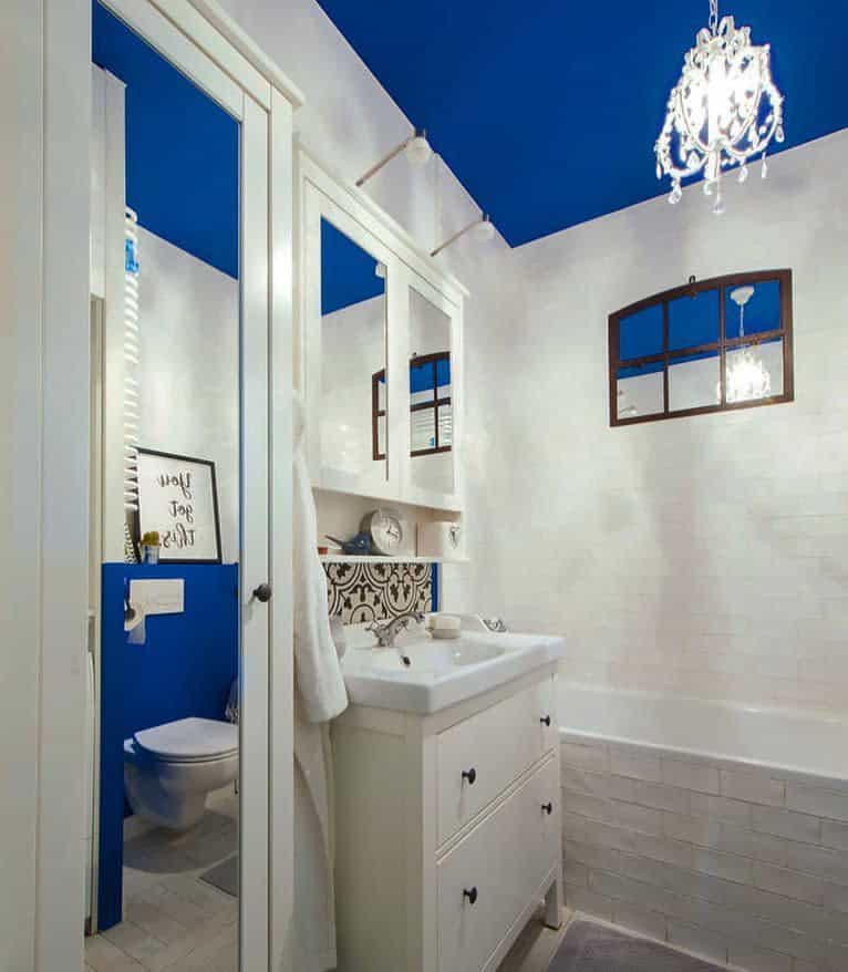 Charming bathroom with a bold blue ceiling, white subway tiles, and a crystal chandelier, creating a striking contrast with a vintage touch.