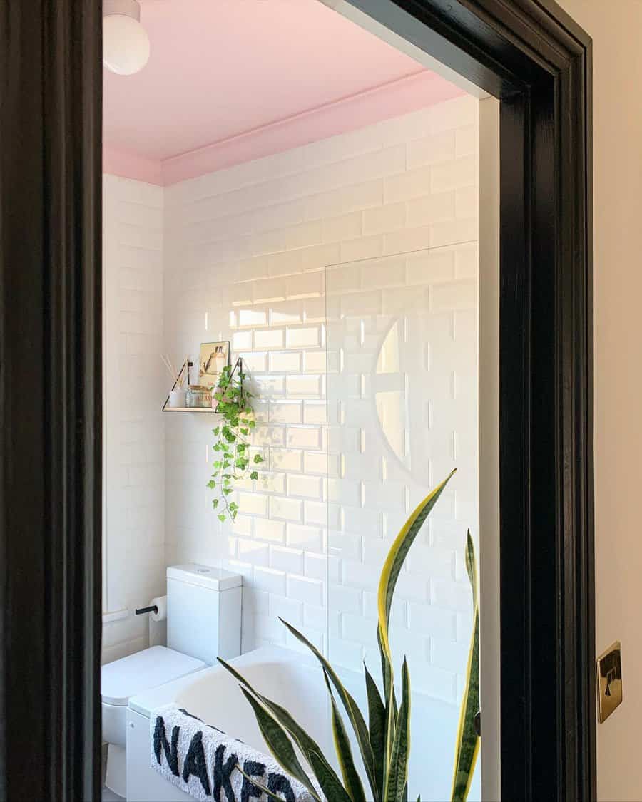 Bright bathroom with a soft pink ceiling, glossy white subway tiles, and black accents, creating a playful yet modern contrast with greenery.