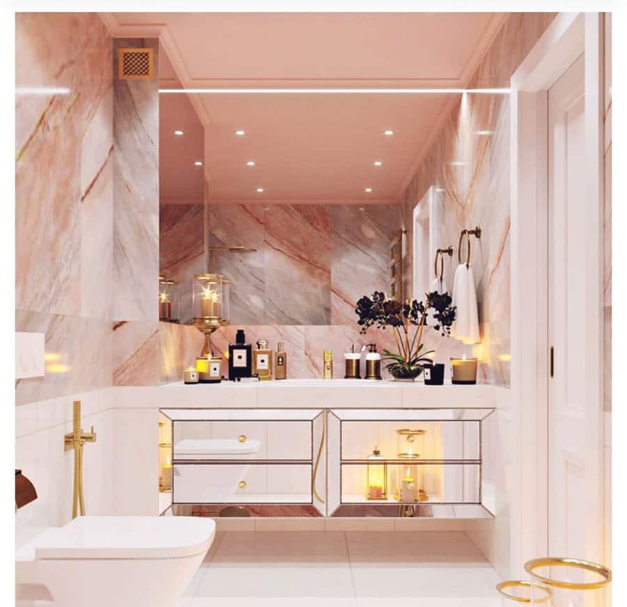 Luxurious bathroom with a soft pink ceiling, marble walls, gold accents, and mirrored cabinetry, creating a glamorous and elegant ambiance.