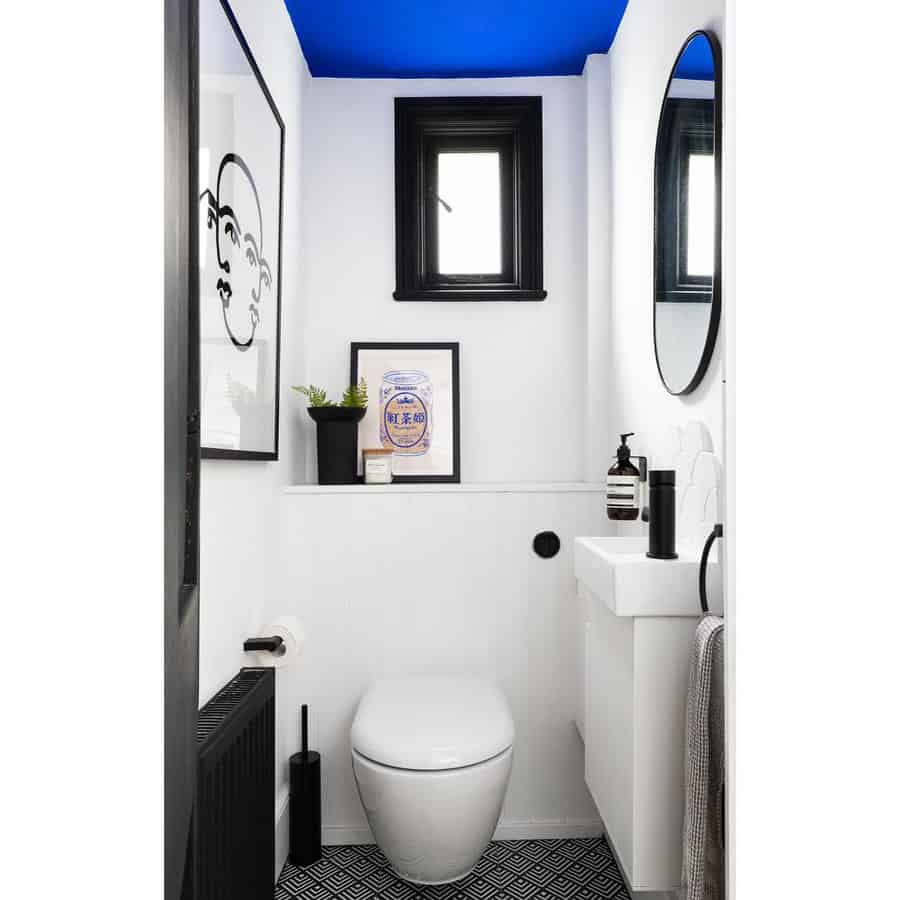 Modern bathroom with a bold blue ceiling, black and white decor, and geometric flooring, creating a striking contrast in a compact space.