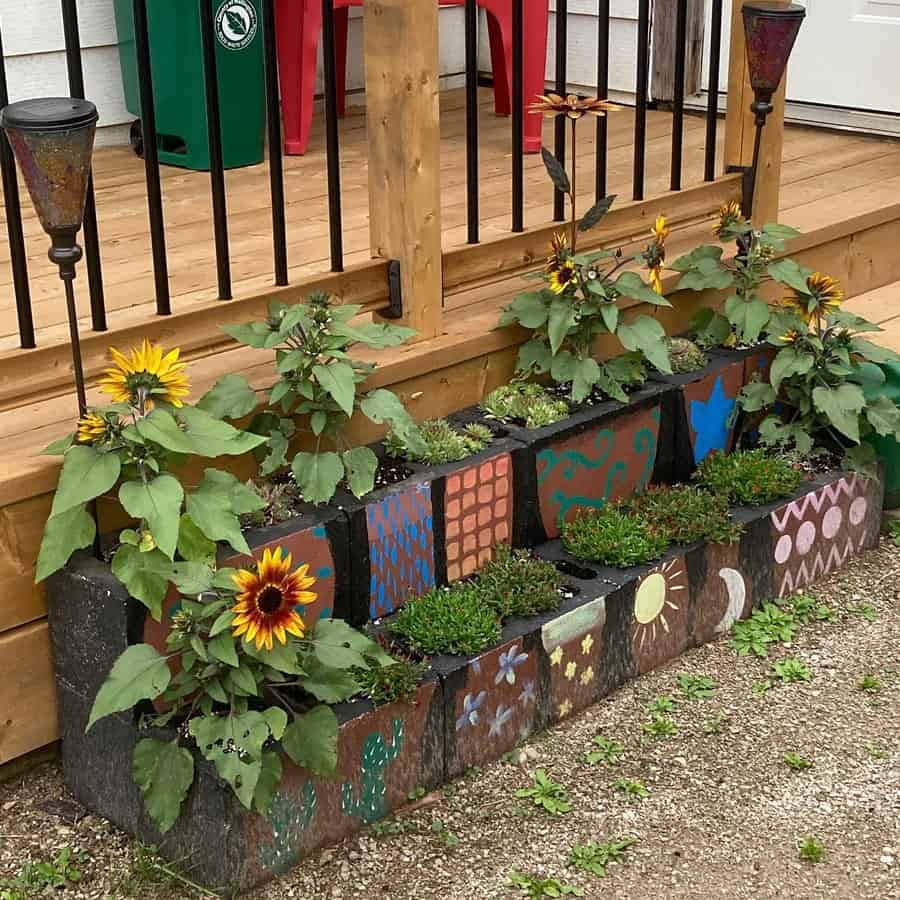 DIY painted cinder block planter with vibrant hand-painted designs, filled with sunflowers and greenery, creating a charming and artistic garden border