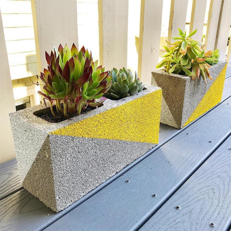 Modern DIY cinder block planters with geometric yellow and gray designs, filled with succulents, creating a stylish and minimalist outdoor decor piece