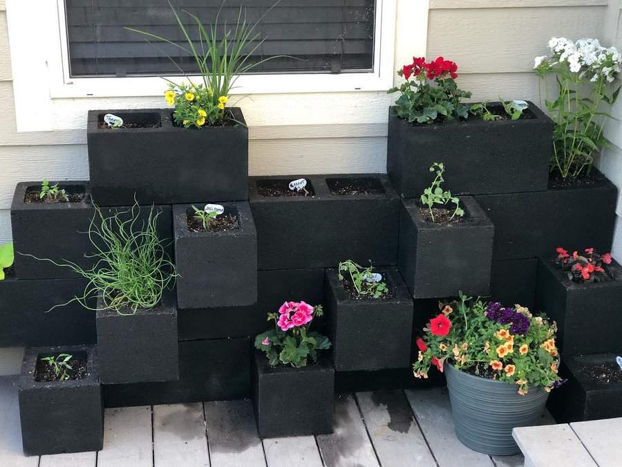 Modern DIY cinder block planter wall painted black, arranged in a tiered design, and filled with colorful flowers and herbs for a stylish outdoor display