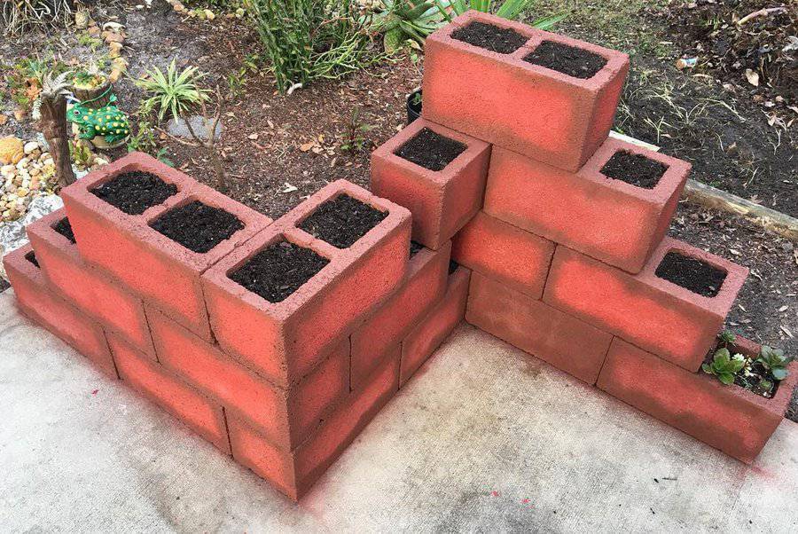 DIY red-painted cinder block planter arranged in a tiered corner design, ready for planting, creating a structured and decorative garden bed