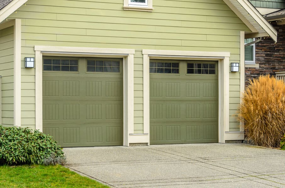 Dual green garage doors on a beige house with landscaping