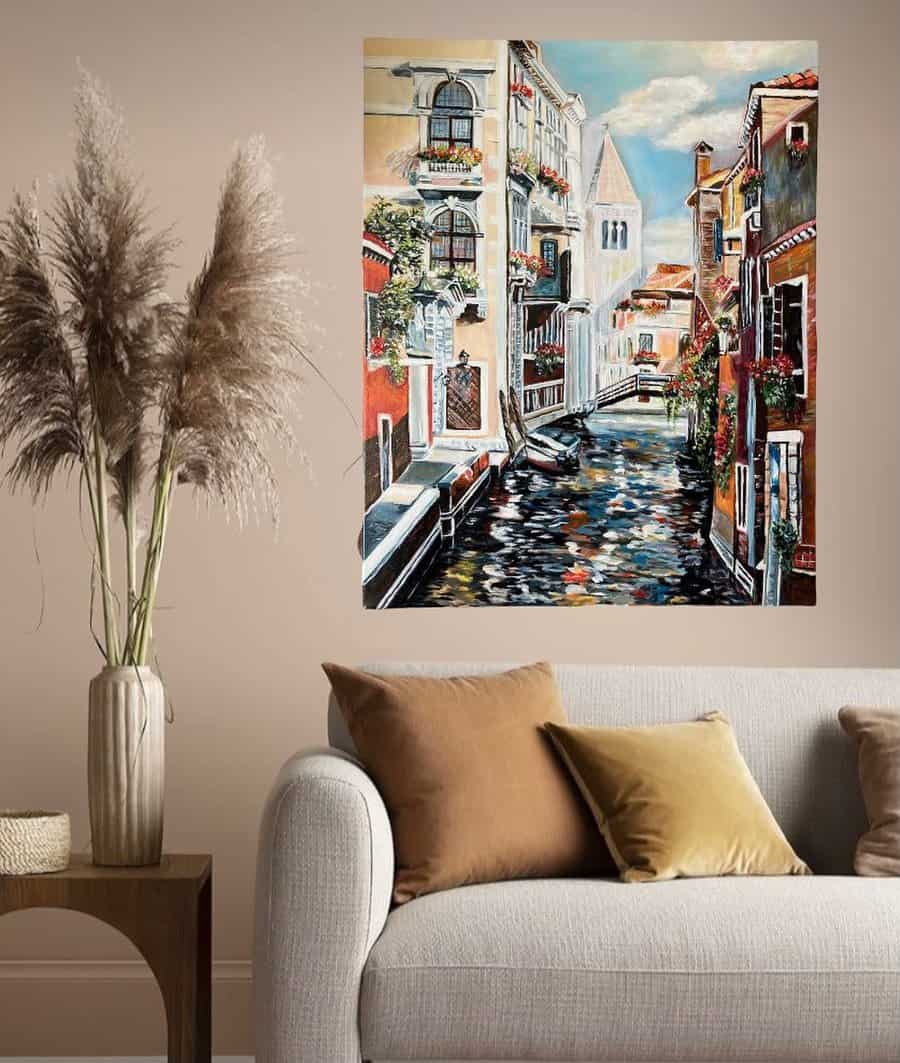 Painting of a Venice canal hung on beige wall above grey sofa and side table with pampas