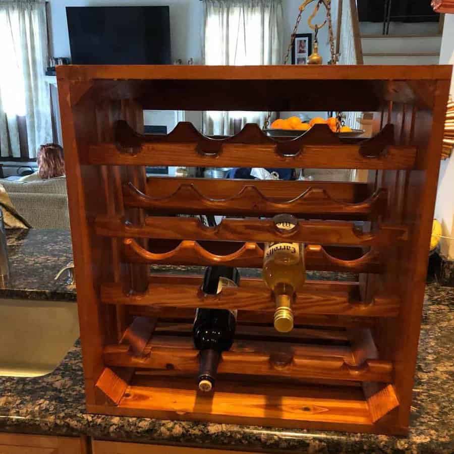 Wooden wine rack on a kitchen counter, holding three wine bottles, with a living room in the background