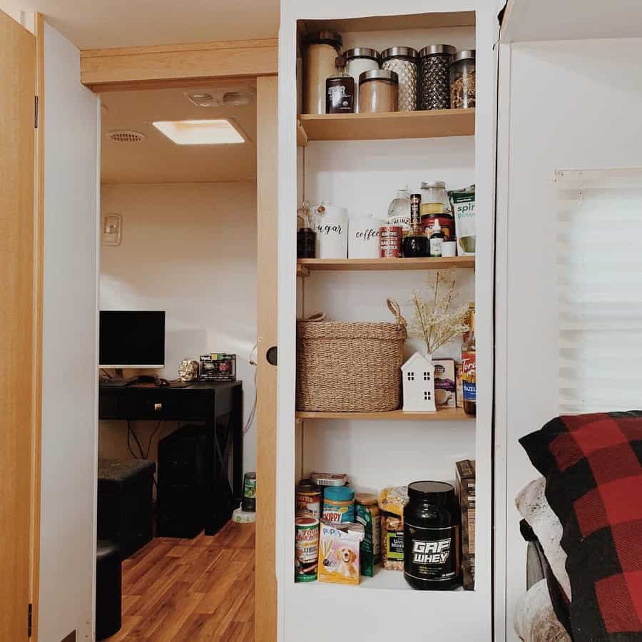 Organized RV pantry with open shelving, glass jars, woven baskets, and neatly arranged food items, maximizing storage in a small space.