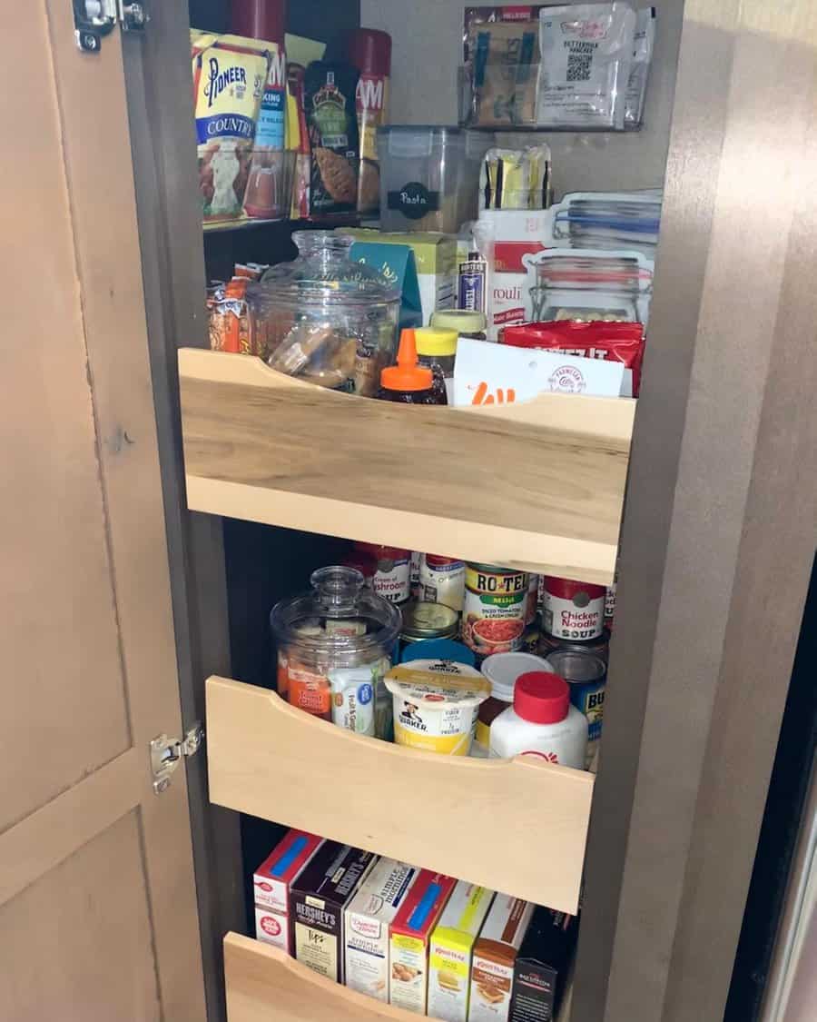 RV pantry with pull-out wooden shelves, neatly organized canned goods, dry foods, and glass storage jars for efficient small-space storage.