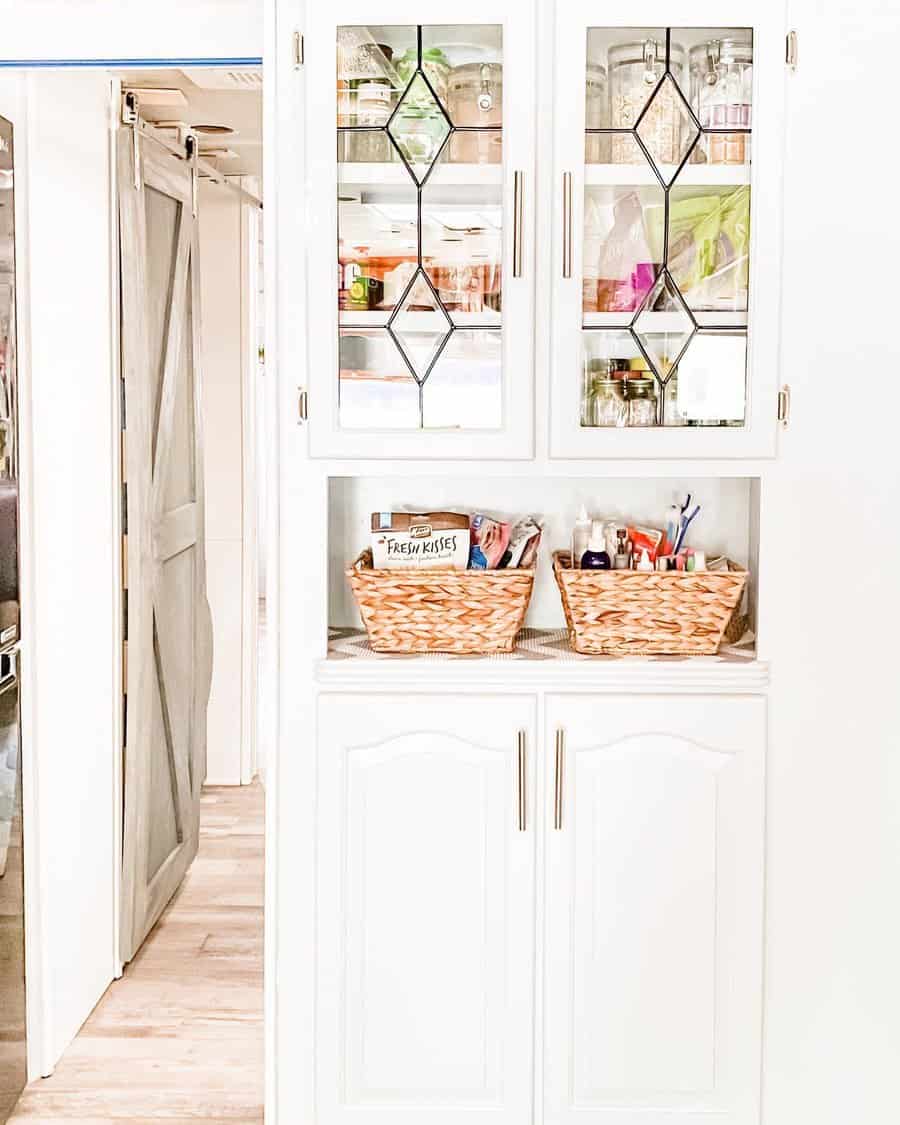 Elegant RV pantry with glass-front cabinets, woven storage baskets, and neatly organized jars, combining style with functional storage.