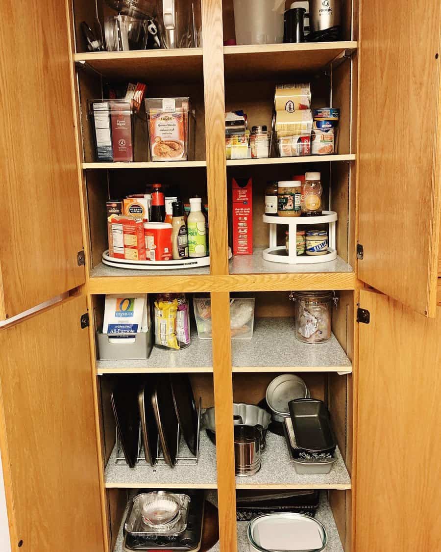 Well-organized wooden pantry with labeled bins, turntables for condiments, and neatly stored baking trays and kitchen essentials