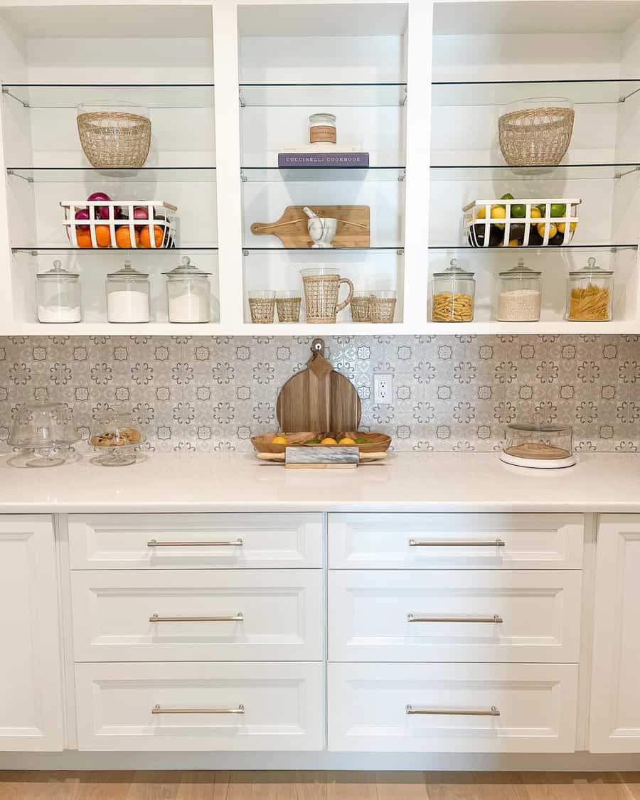 Elegant kitchen with white cabinetry, glass shelves, woven baskets, labeled jars, and a decorative backsplash for a clean, modern look