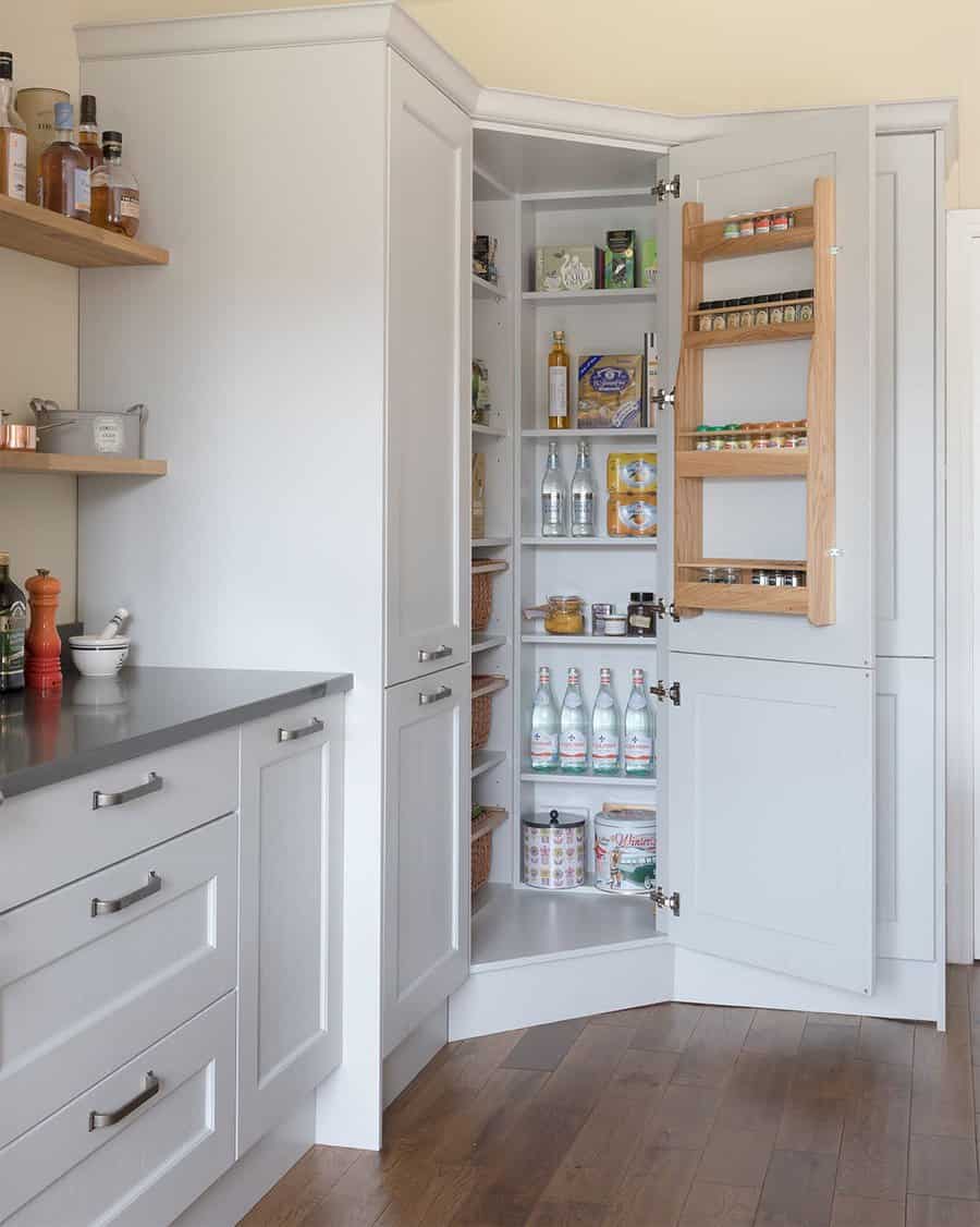 Elegant corner pantry with built-in spice racks, neatly arranged shelves, and soft gray cabinets for a stylish and efficient kitchen storage