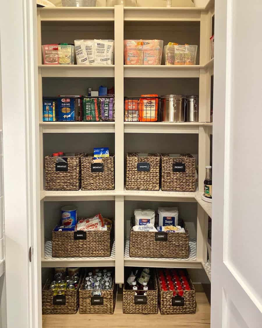 A neatly organized pantry with labeled wicker baskets and shelves stocked with various food items, snacks, and drinks