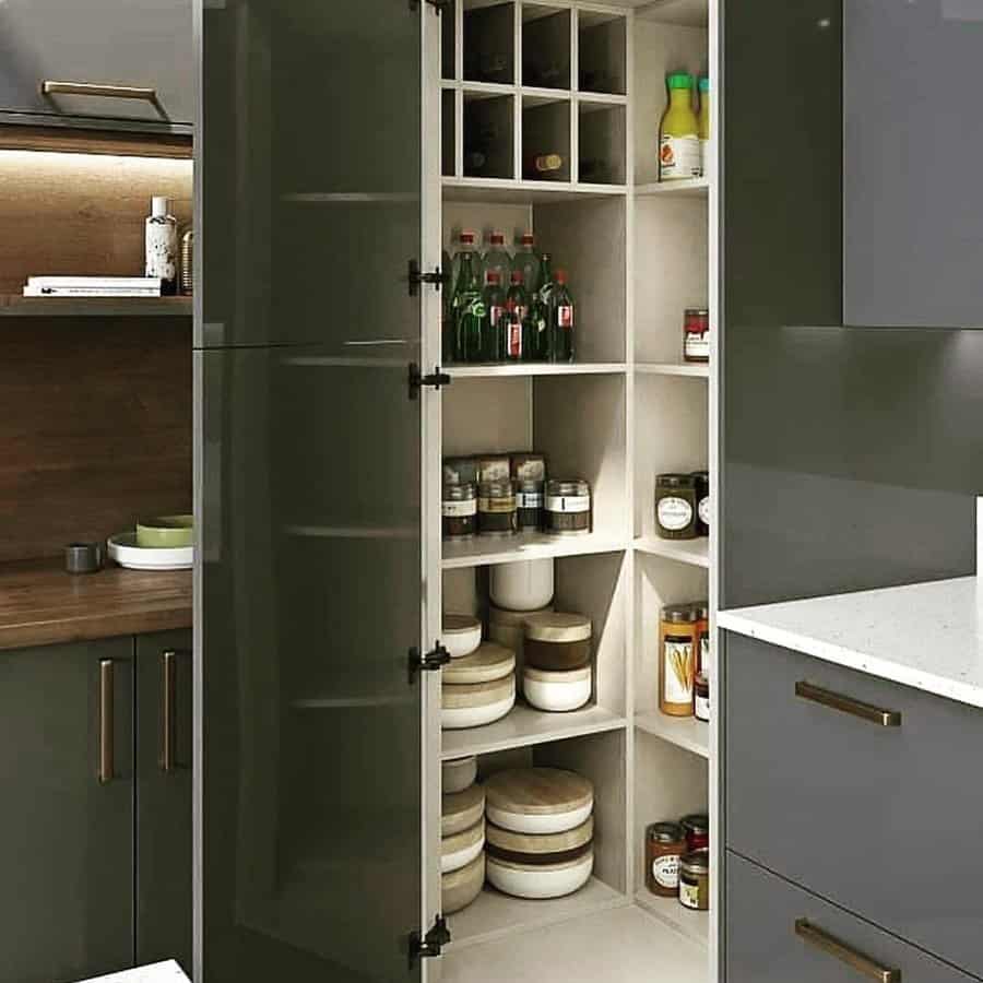 Modern kitchen pantry with neatly organized shelves containing jars, bottles, and containers, featuring dark cabinets and a white countertop