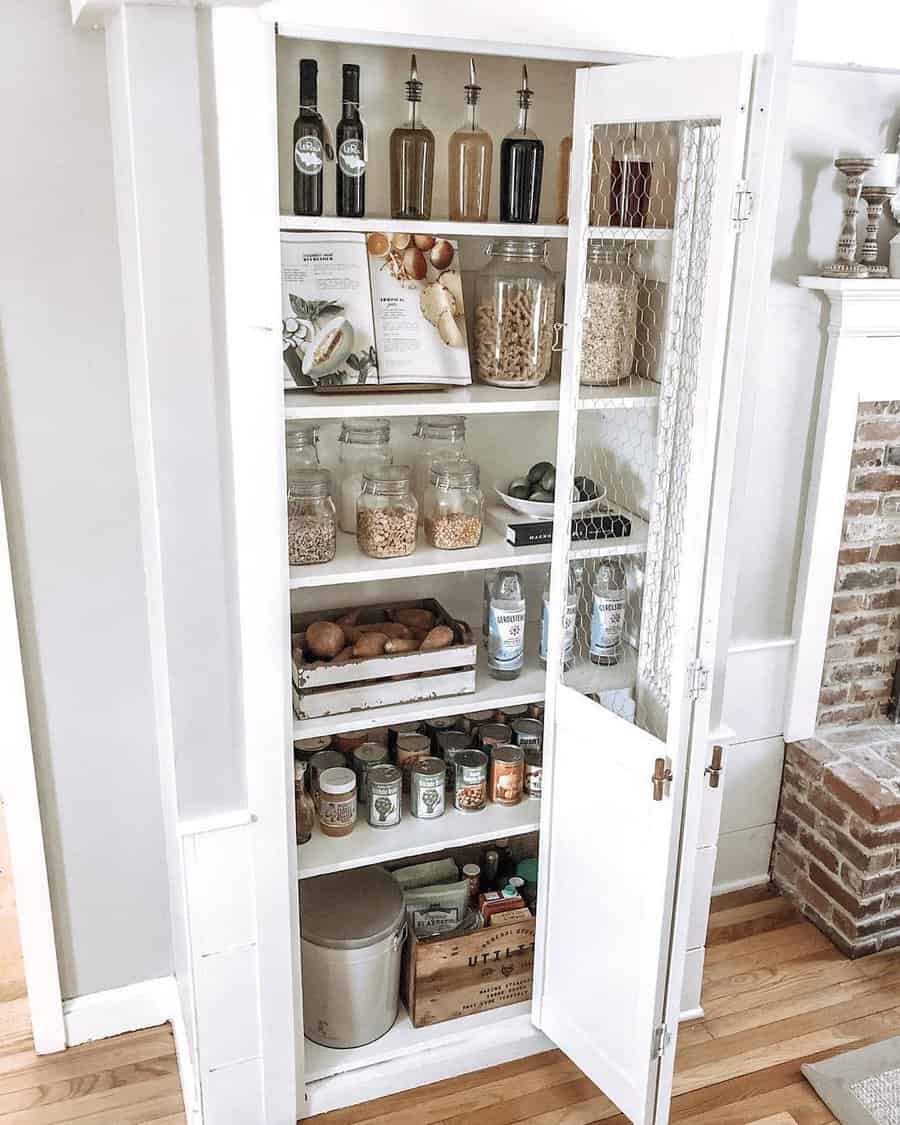 A neatly organized pantry with jars of grains, canned goods, and bottles of oil in a white cabinet with a wire mesh door