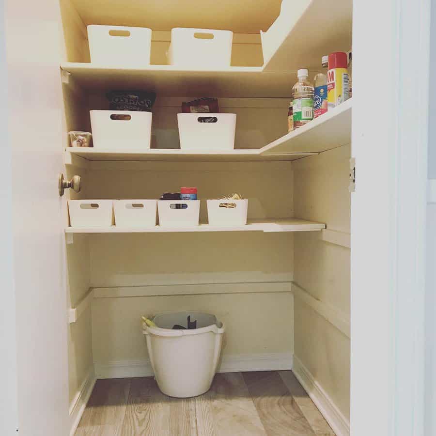 Kitchen pantry with white shelves, organized with white bins and various items, and a trash bin on the floor