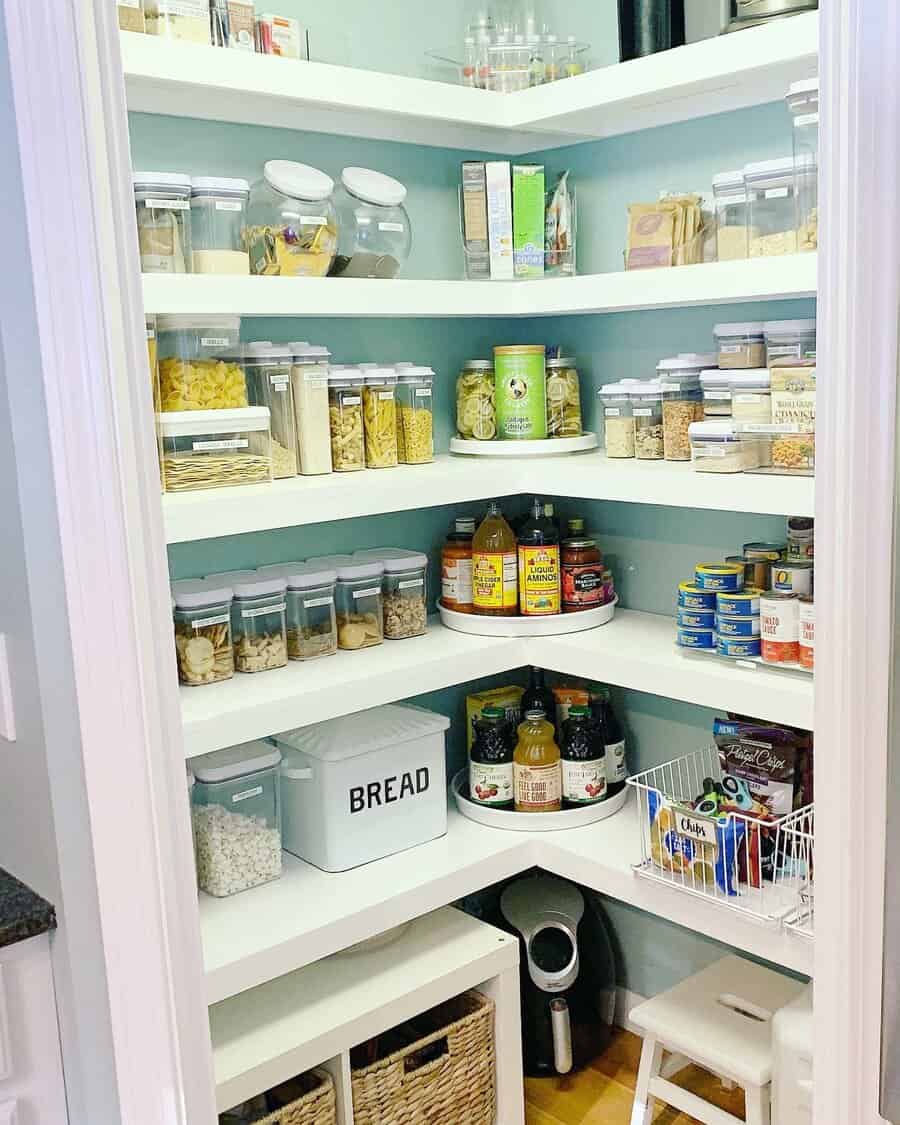 Organized pantry with clear containers, canned goods, pasta, cereals, and a bread box on white shelves