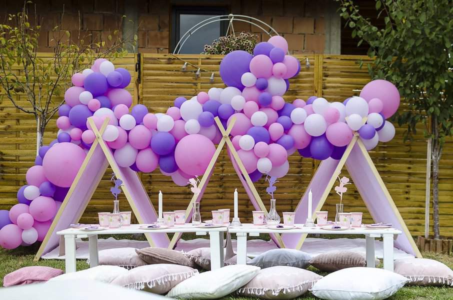 Outdoor picnic setup with pink and purple balloons, small tents, low tables, and cushions: perfect for a festive gathering