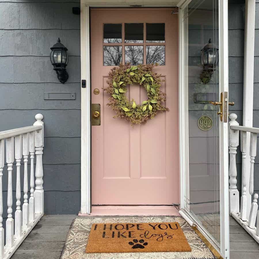 A pink front door with a wreath, a glass storm door, and a doormat that reads "I hope you like dogs" with a paw print