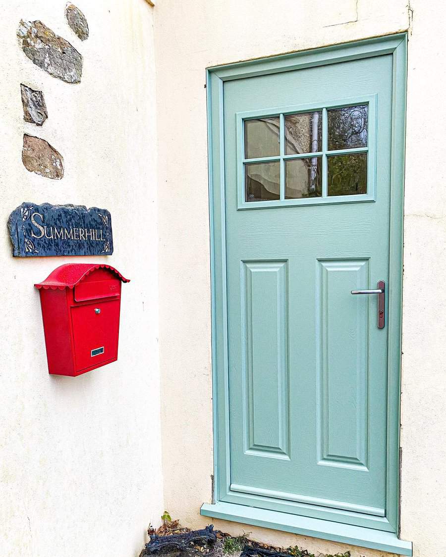 A mint green door with glass panes, next to a red mailbox, and a plaque reading "Summerhill" on a cream wall