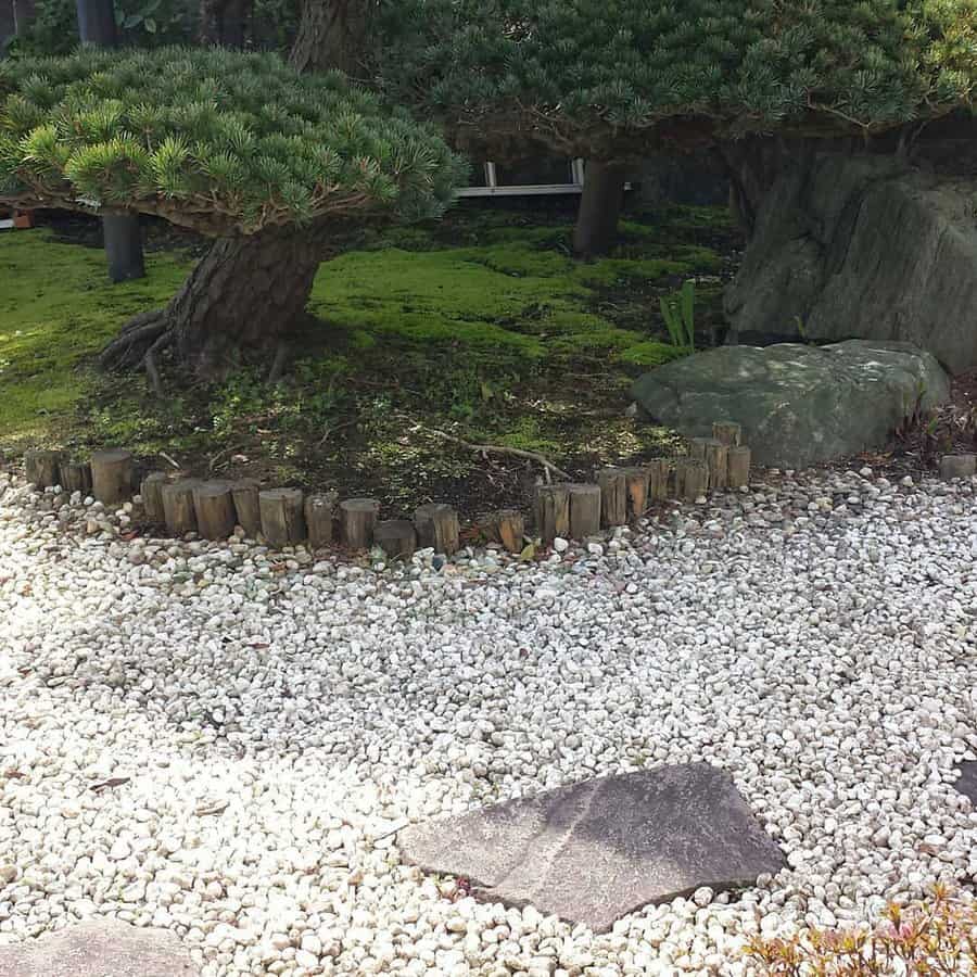 Japanese garden with moss, a stone path, and manicured trees, bordered by small wooden posts