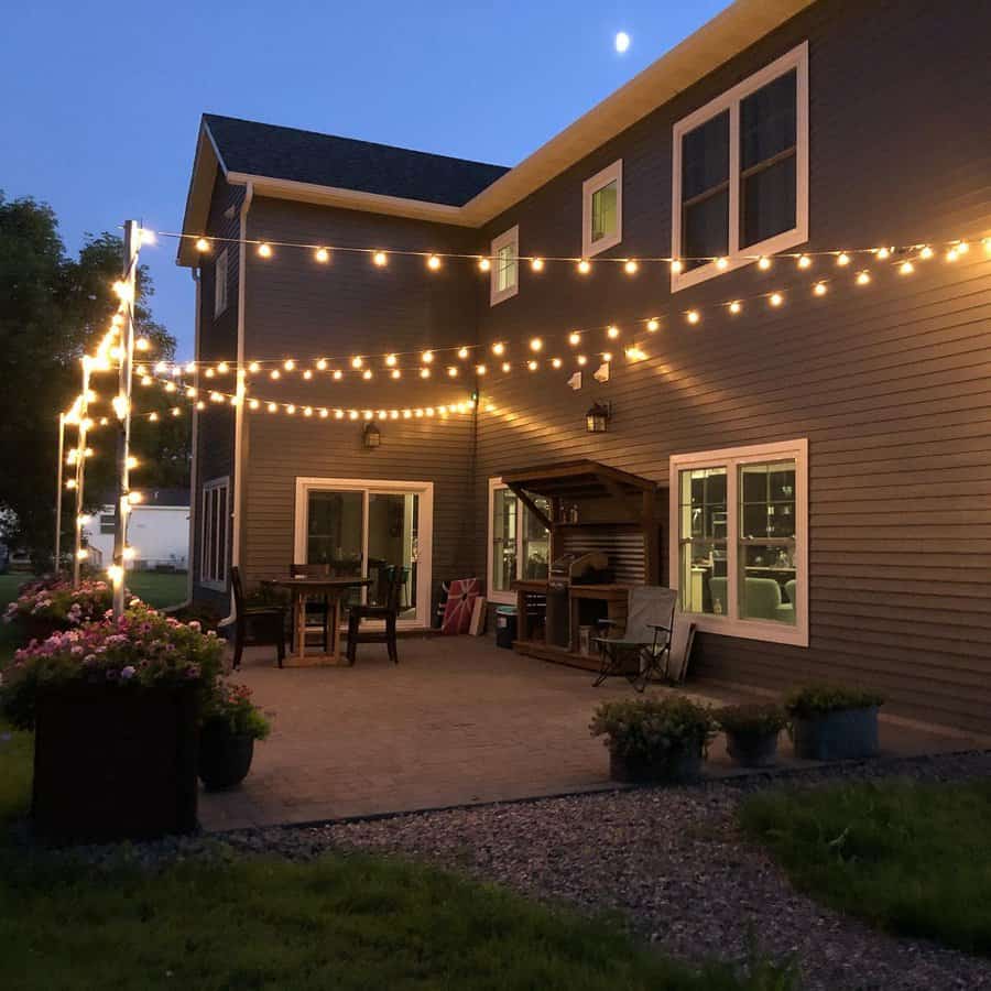 Cozy backyard patio at dusk, adorned with string lights, surrounded by a garden, with a table and chairs for relaxing