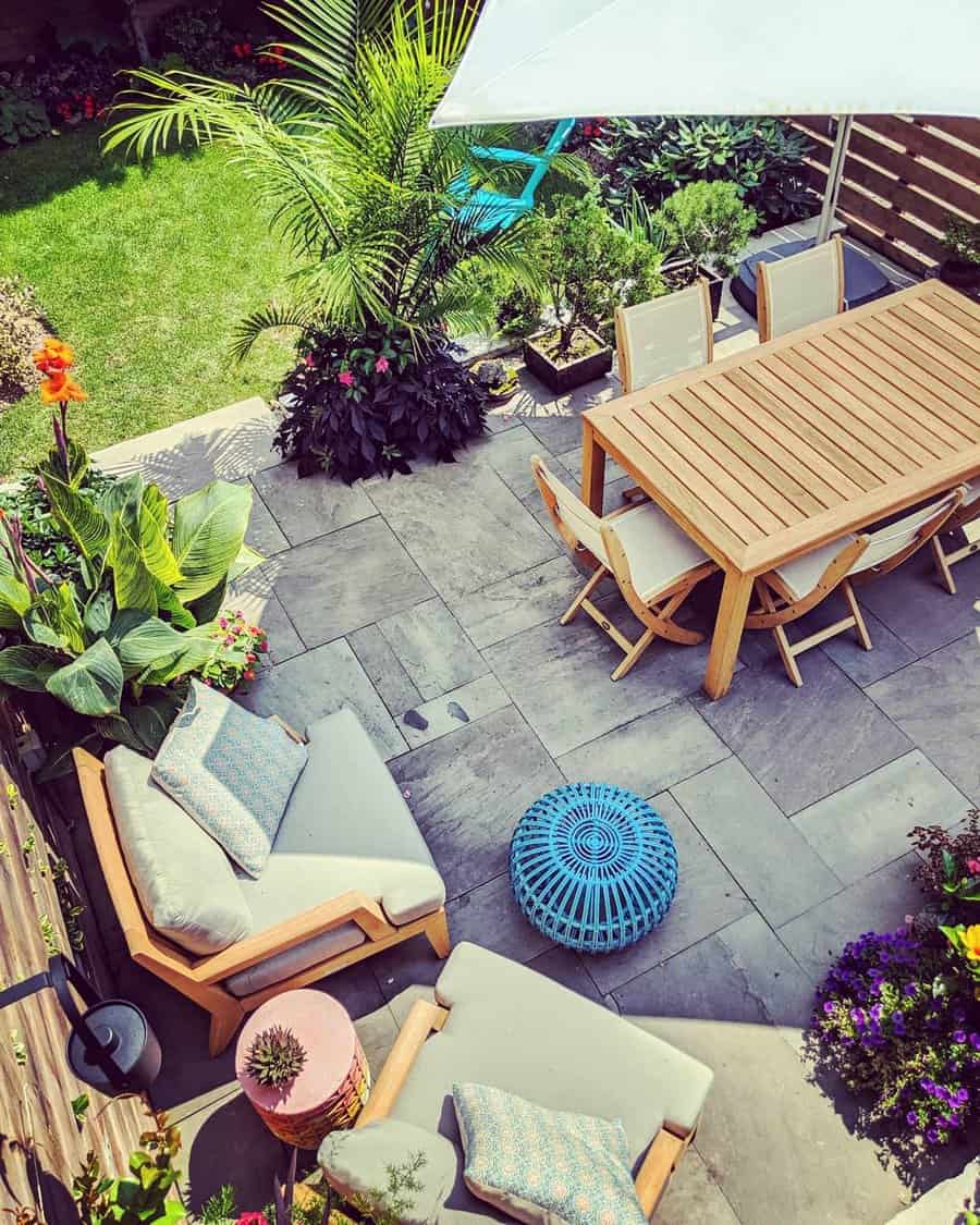 Aerial view of a garden patio with wooden dining and lounge furniture, plants, and a blue pouf under a white umbrella