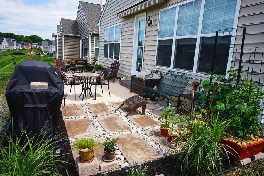 Cozy backyard patio with a mix of stone pavers and gravel, outdoor seating, a grill, and lush potted plants for a charming and functional space