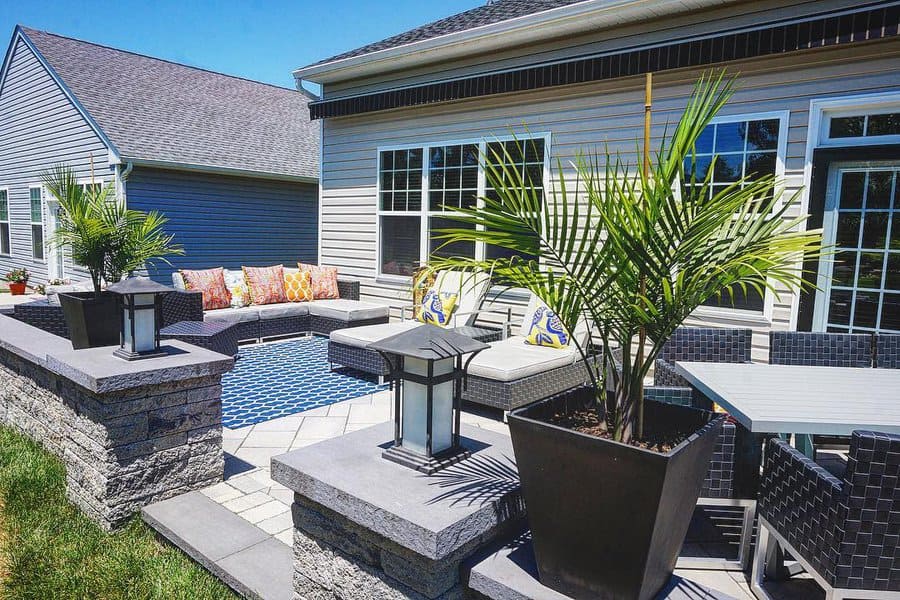 Modern backyard patio with sleek stone pavers, built-in seating, vibrant cushions, tropical plants, and stylish lighting for a cozy outdoor retreat