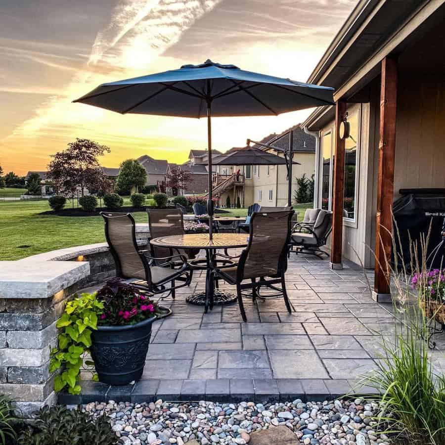 Beautiful backyard patio with elegant stone pavers, a shaded dining area, cozy seating, and lush landscaping for a perfect outdoor retreat