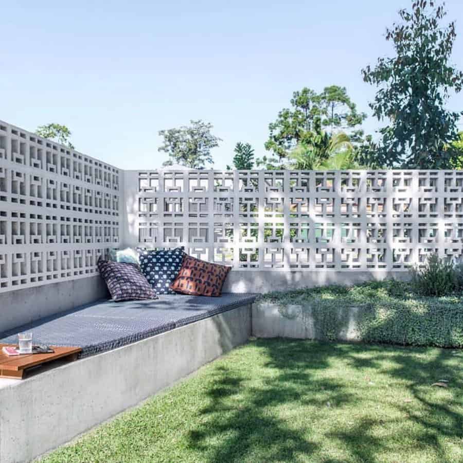 Modern outdoor lounge area with a built-in concrete bench, decorative cinder block privacy wall, and cozy cushions, creating a stylish backyard retreat