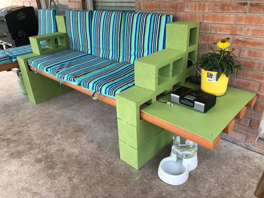 DIY outdoor cinder block bench painted green, featuring striped cushions, built-in side tables, and storage, creating a cozy and functional patio seating area