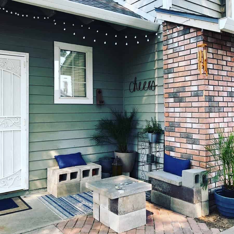 Cozy front porch seating area with DIY cinder block benches, a matching table, blue cushions, and potted plants, creating a welcoming outdoor retreat