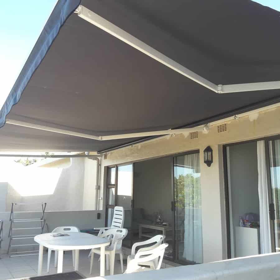 A patio with a retractable awning, white plastic table, and chairs; glass sliding doors lead to the interior