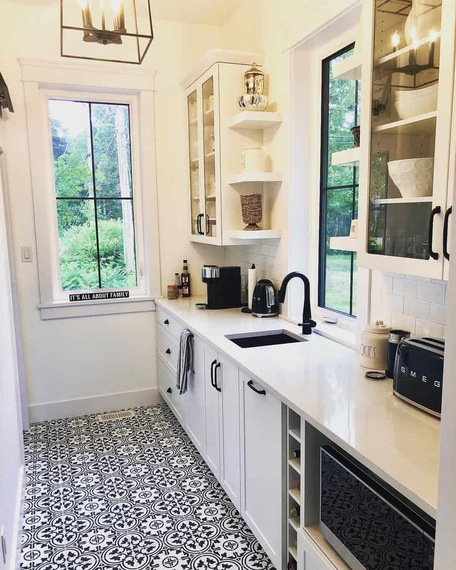 Narrow kitchen with white cabinets, black faucet, patterned tile floor, large windows, and modern appliances