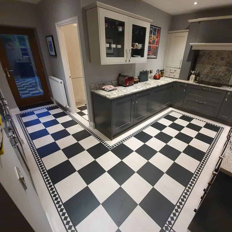 Kitchen with black and white checkered floor, gray cabinets, and a marble countertop, dark wooden door in the background