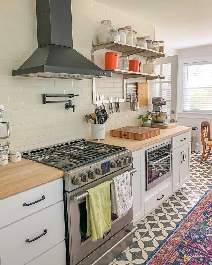 Black-and-white patterned tile flooring adds a vintage charm to this bright, farmhouse-style kitchen, complementing wood countertops and open shelving