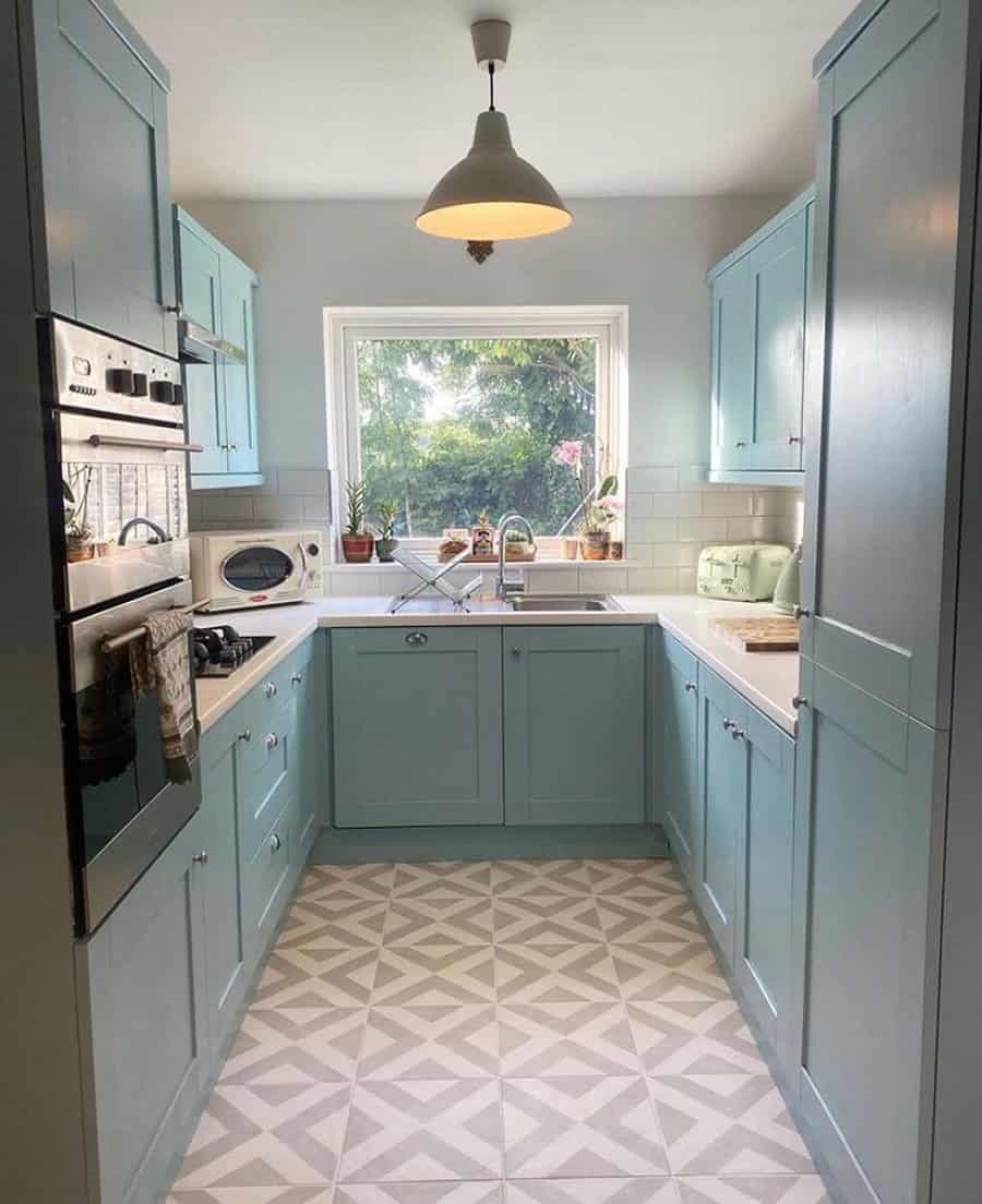 Geometric patterned tile flooring adds a stylish touch to this charming blue kitchen, enhancing its vintage-inspired design and bright, airy feel