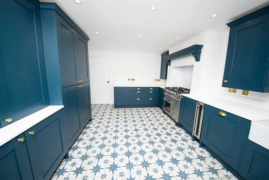 Kitchen with blue cabinets, star-patterned floor tiles, white walls, and stainless steel oven. Bright lighting and minimalist design