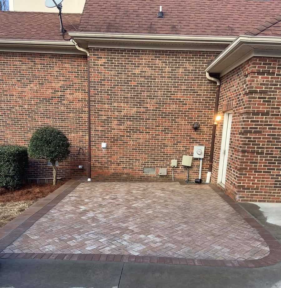 Herringbone brick patio against a brick wall with landscaping