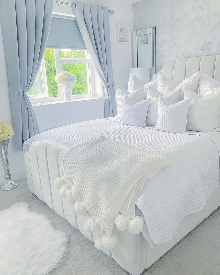 Bright bedroom with a white bed, multiple pillows, and a pom-pom throw