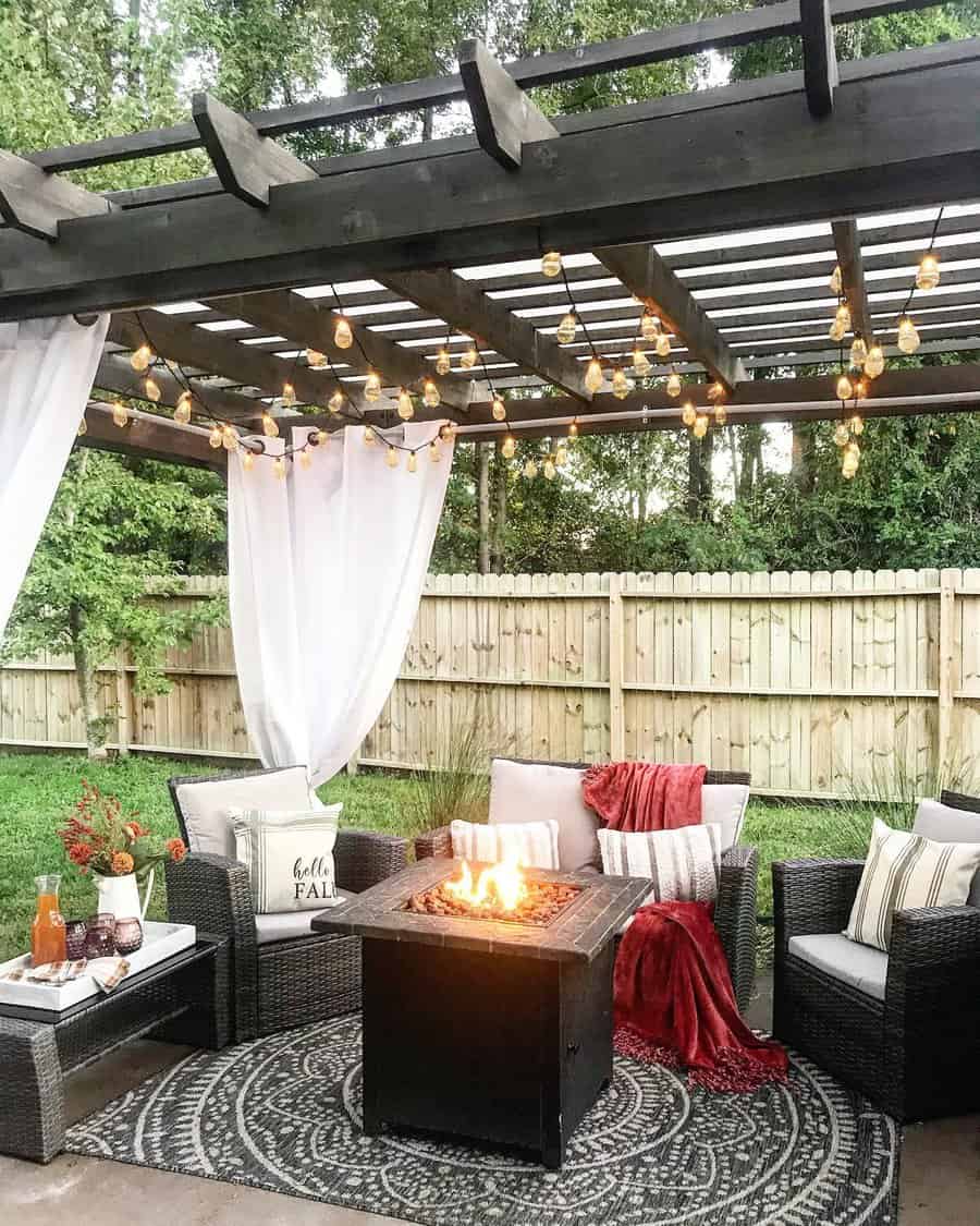 Cozy patio with a fire pit, seating, string lights, and a pergola, decorated with pillows, a red blanket, and fall-themed accents