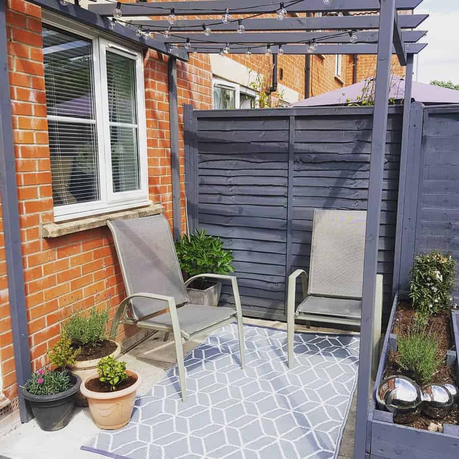 Small patio with a pergola, string lights, privacy fencing, metal chairs, potted plants, and a geometric outdoor rug for a cozy retreat