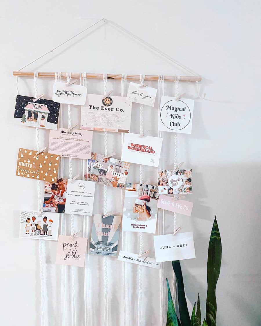 A wall hanging with a wooden rod displaying various cards and photos clipped on strings