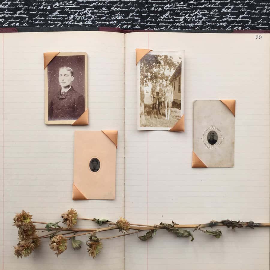 Open notebook with vintage photos and dried flowers on pages, against a backdrop of cursive writing