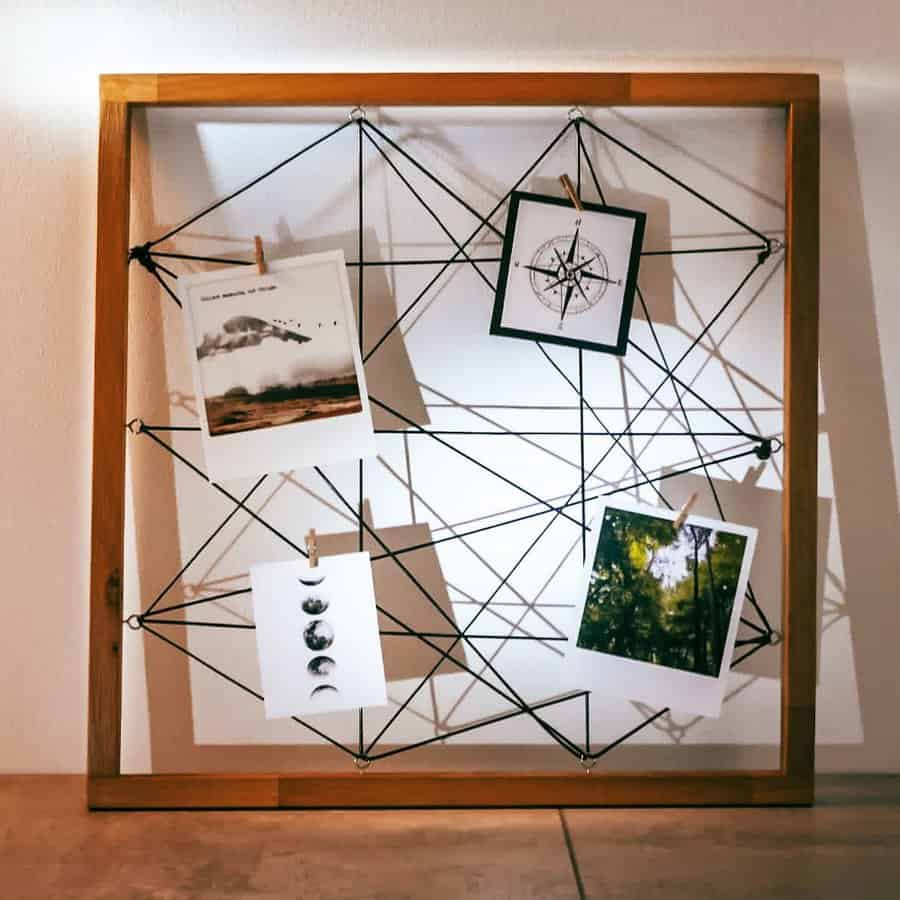 Wooden frame with black string in a geometric pattern, holding four photos with small clothespins