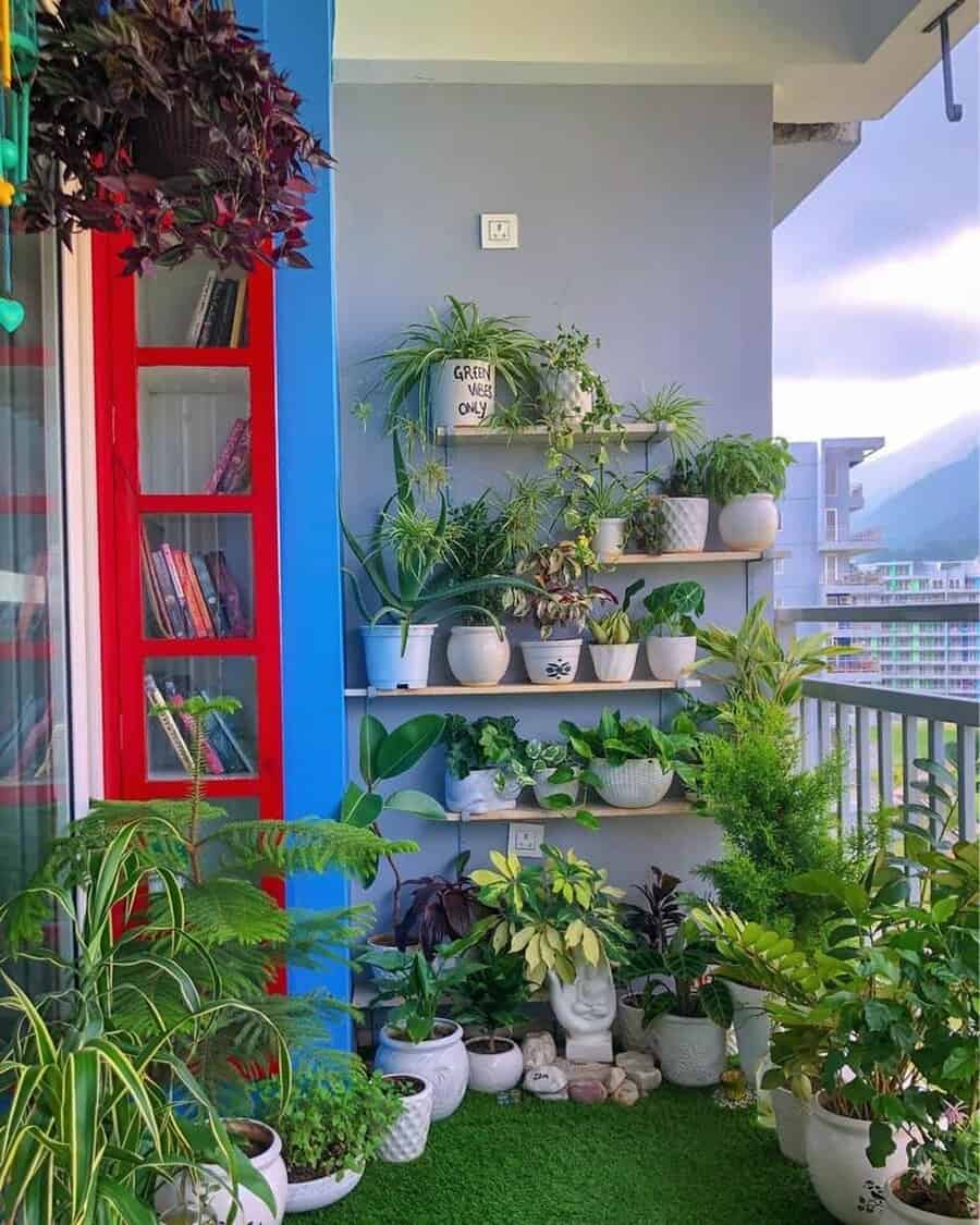 Balcony garden with various potted plants on shelves and floor, red window frame, and cityscape in the background