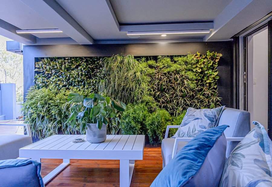 Modern patio with a lush green living wall, sleek white furniture, blue accent pillows, and warm wooden flooring